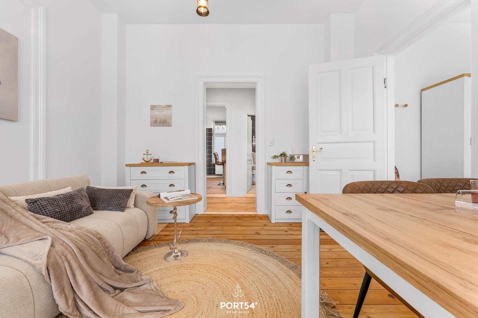 Wohn- und Essbereich mit Sofa, Holztisch und Schubladenkommoden.