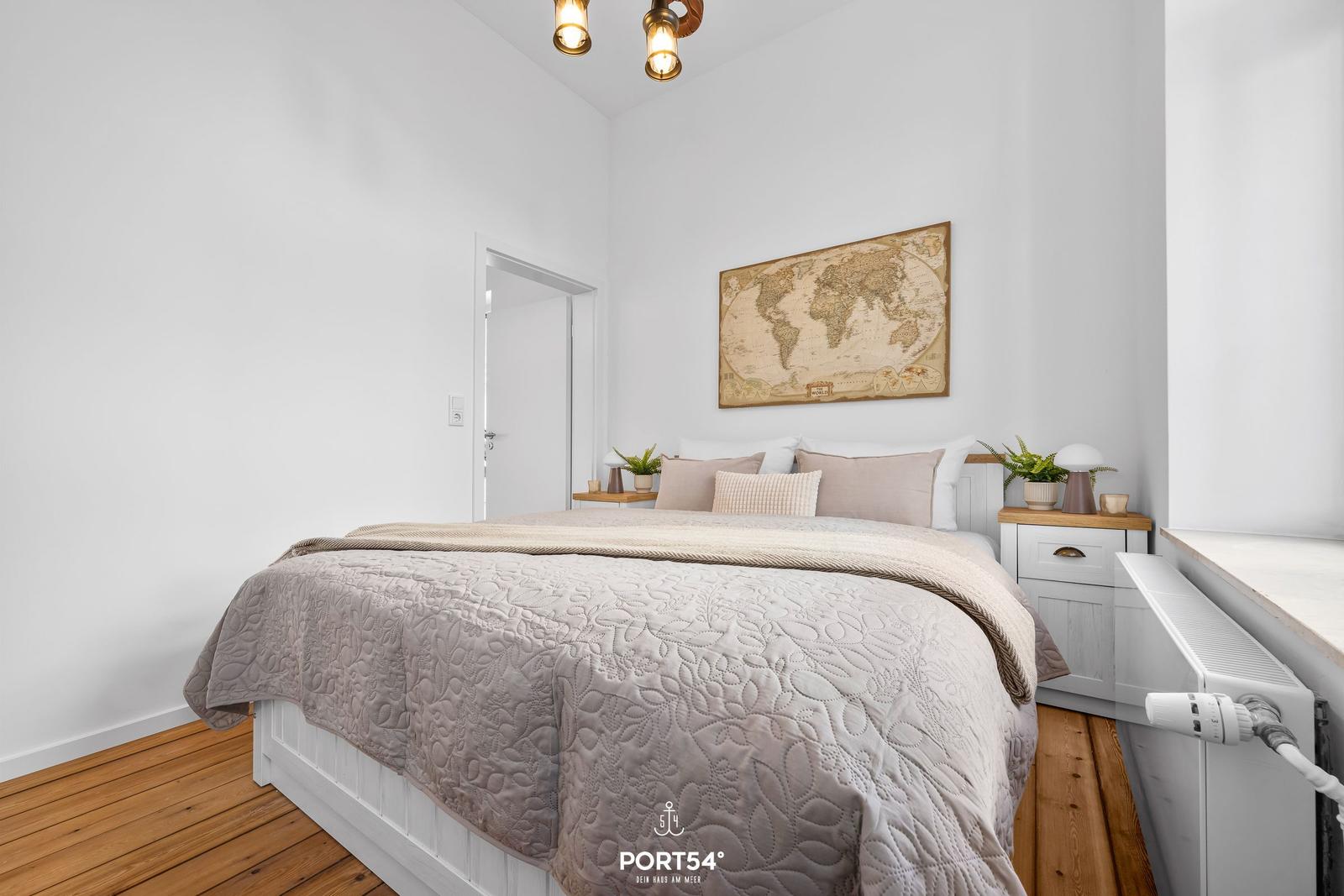 Schlafzimmer mit Bett, Nachttisch und Weltkarte an der Wand.