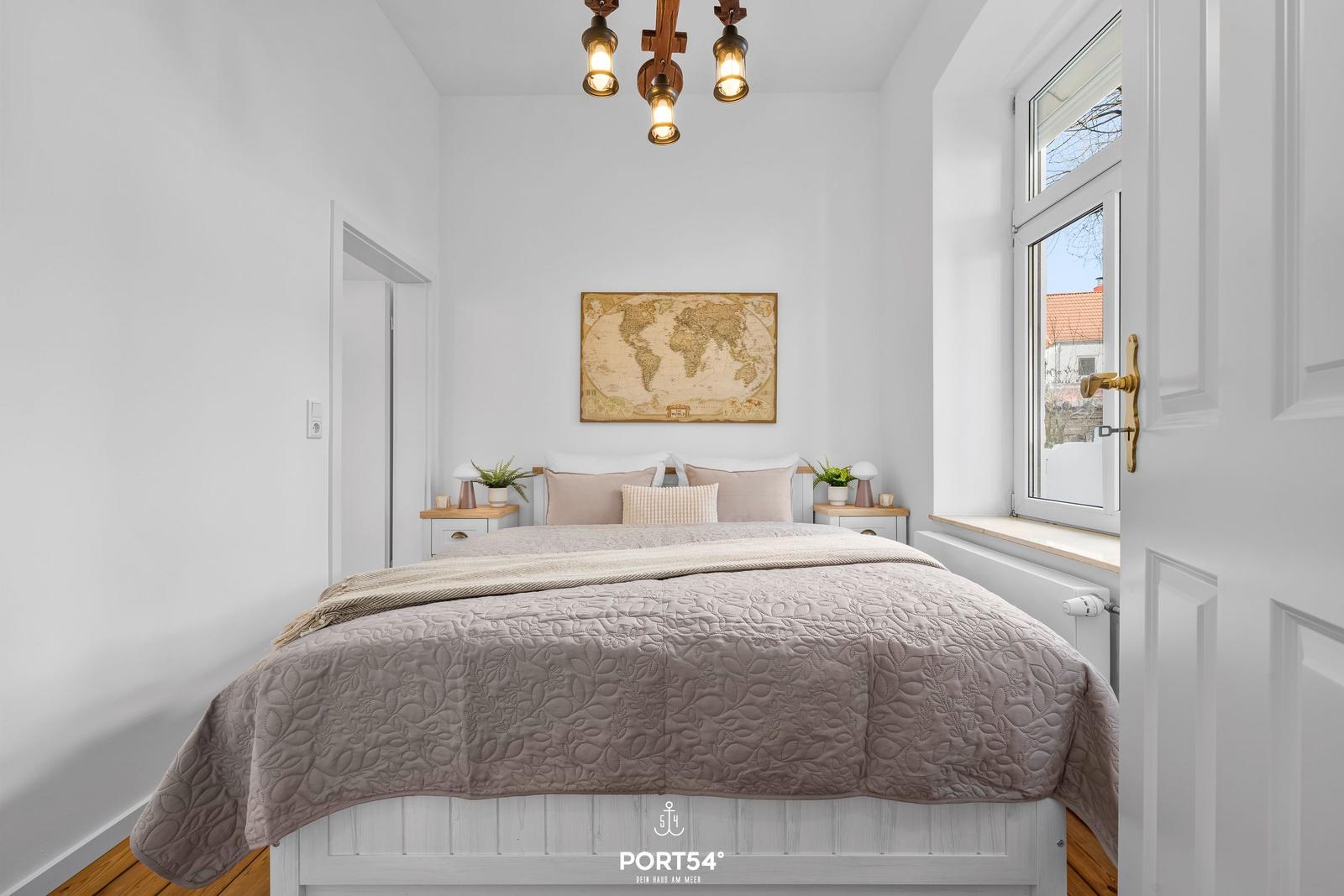 Schlafzimmer mit Bett, Wandkarte und Fenster. Holzfußboden und Deckenleuchte.