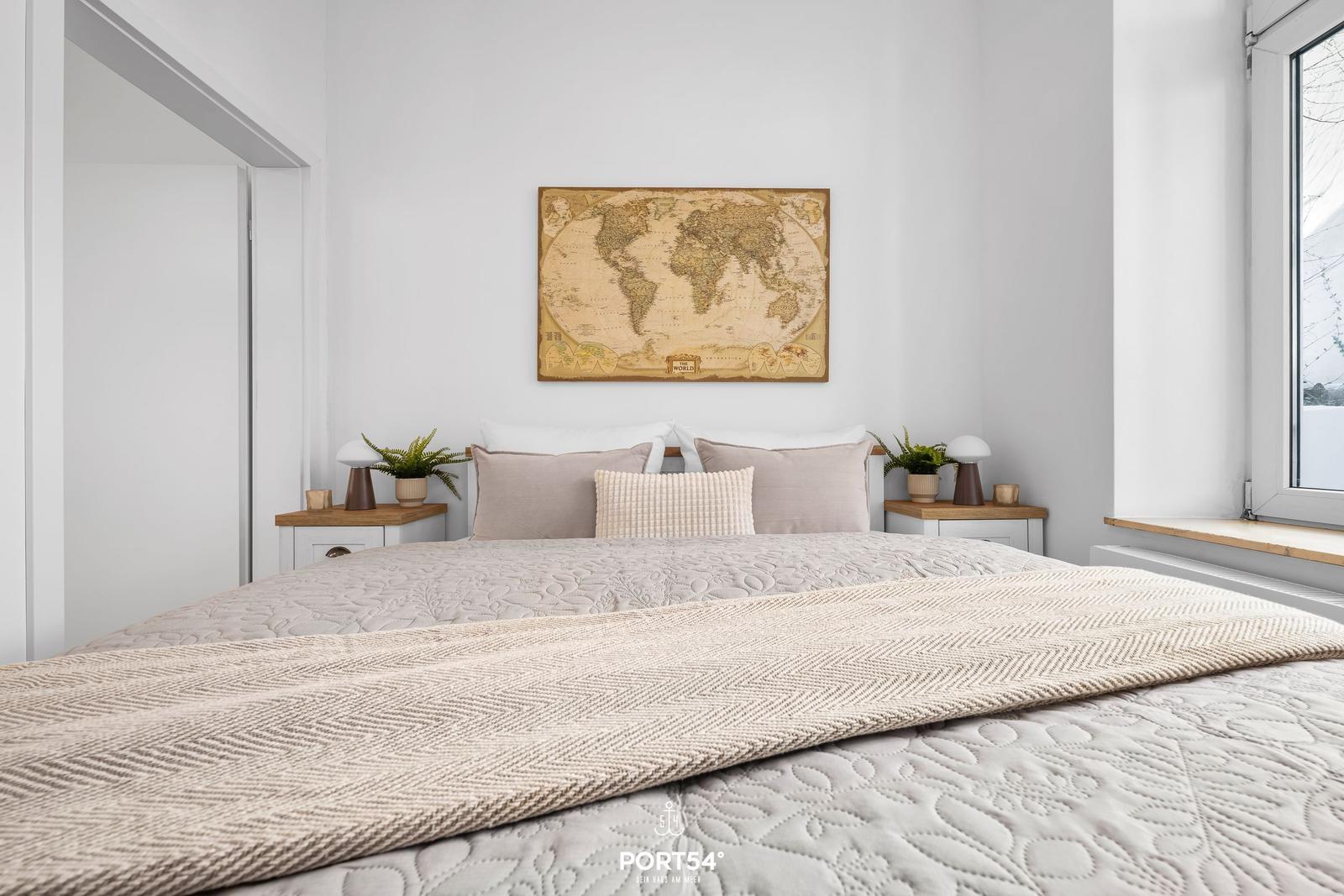 Schlafzimmer mit Bett, Nachttischen und Weltkarte an der Wand.