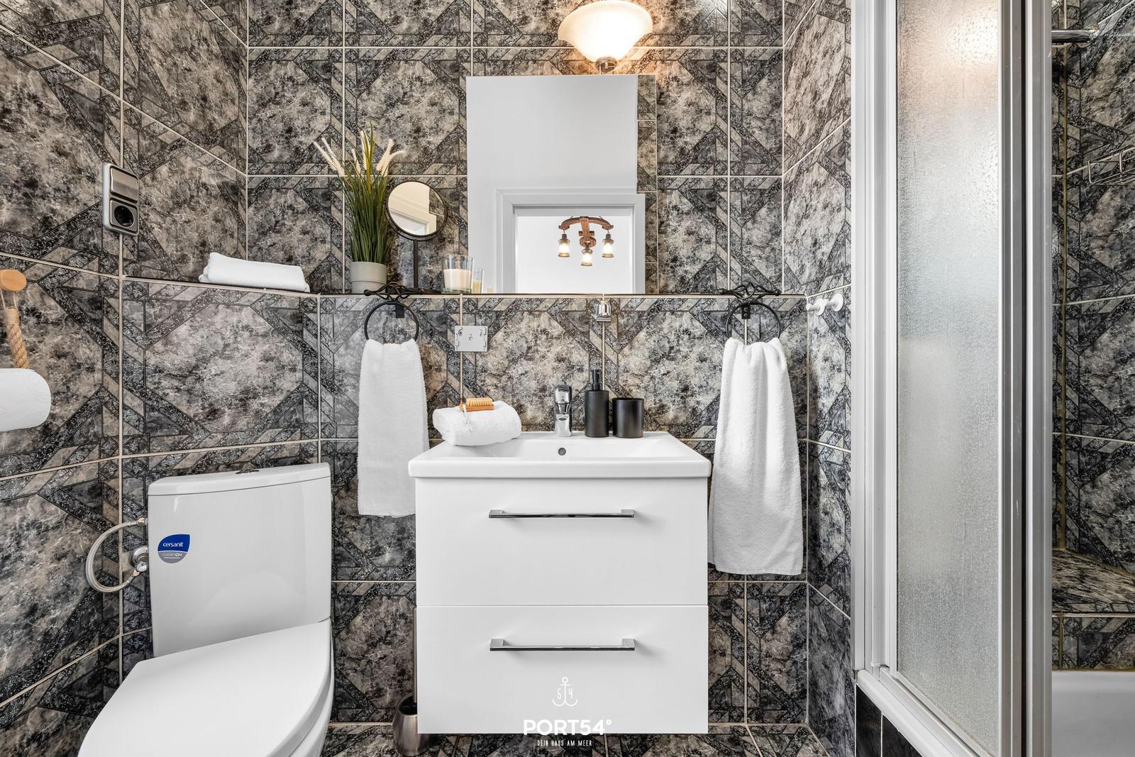 Badezimmer mit Marmorfliesen, Waschbecken, Toilette und Dusche