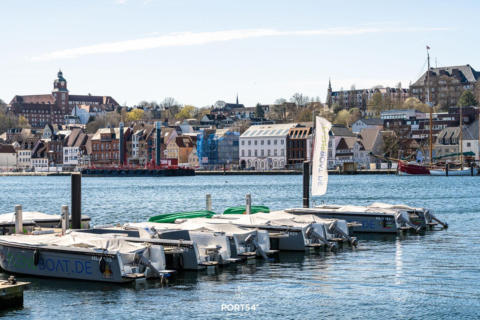Hafen mit Bootsanlegern und Blick auf historische Gebäude im Hintergrund.