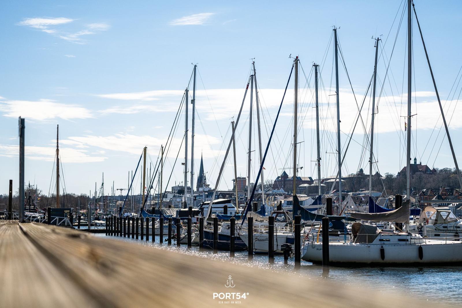 Hafen mit Segelyachten und Blick auf Stadt im Hintergrund.
