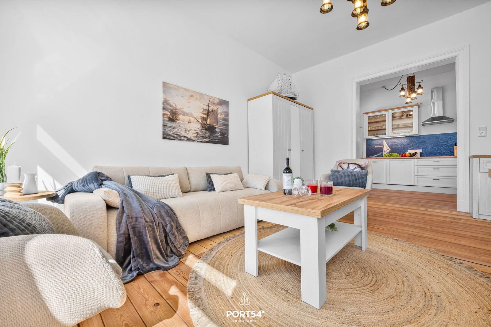 Wohnzimmer mit Sofa, Tisch und Küchenbereich im Hintergrund.