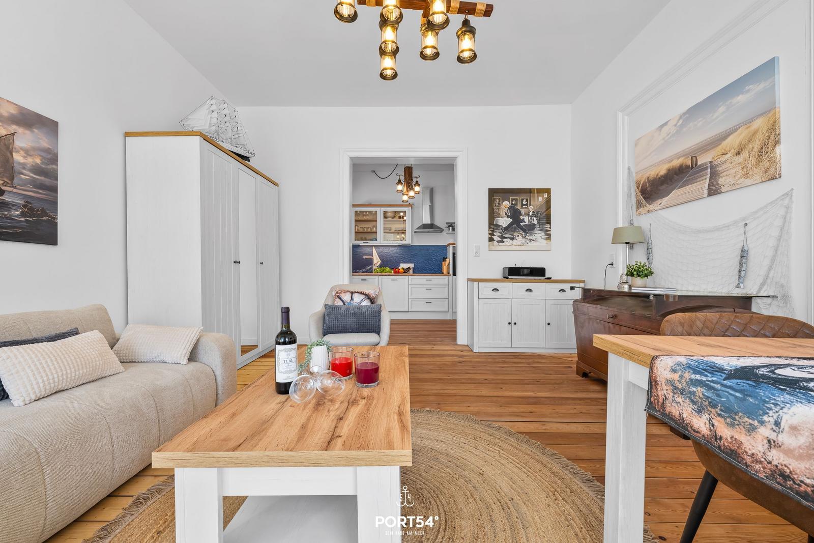 Wohnzimmer mit Holztisch, Sofa und Küchenbereich im Hintergrund.
