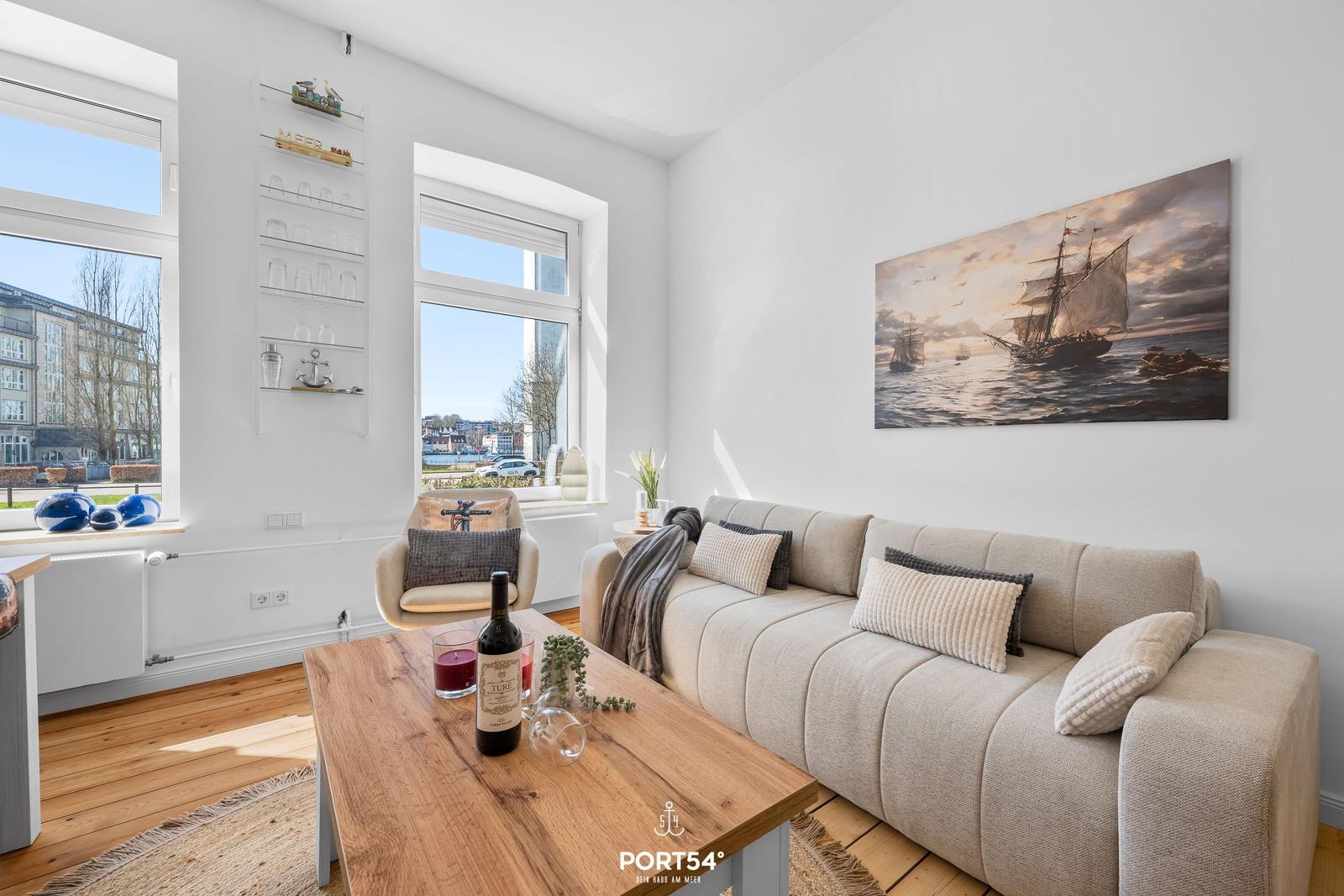 Wohnzimmer mit Sofa, Holztisch und Fensterblick auf die Straße.