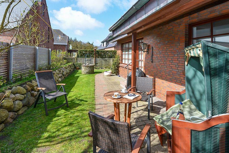 Terrasse mit Garten, Tisch, Stühlen und Liegestühlen. Haus mit Backsteinfassade.