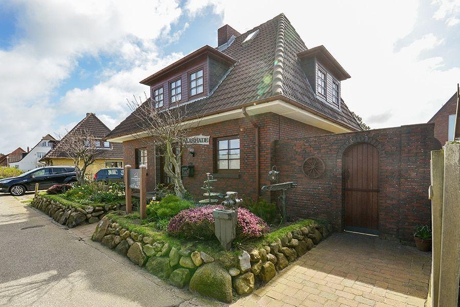 Haus mit Backsteinfassade, Dachgauben und gepflegtem Vorgarten mit Steinmauer.