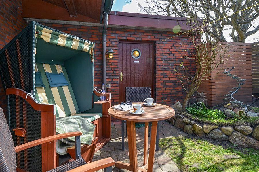 Hinterhof mit Liegestuhl, Tisch und Garten. Backsteinmauer und kleine Pflanzen.