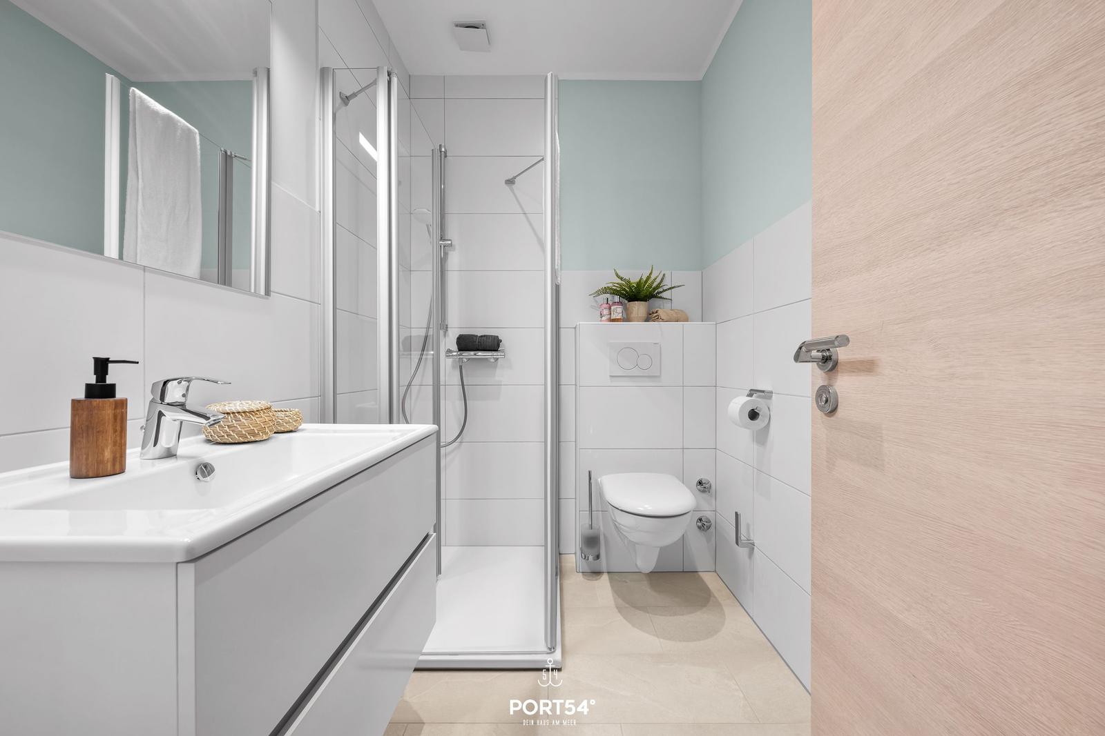 Badezimmer mit Dusche, Waschbecken und Toilette. Holztür und Wandfarbe.