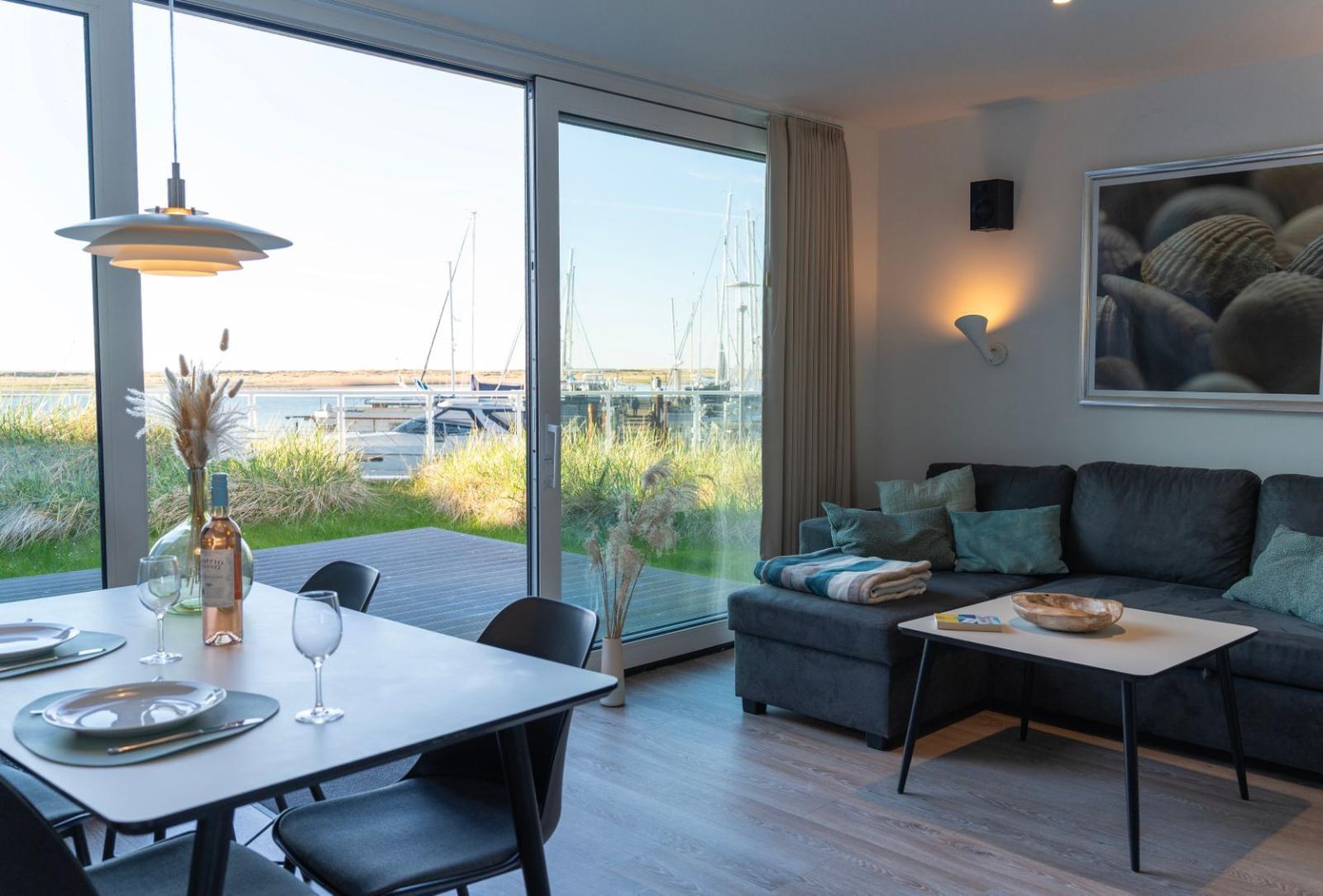 Wohn- und Essbereich mit Blick auf den Hafen. Sofa, Tisch und große Fenster.