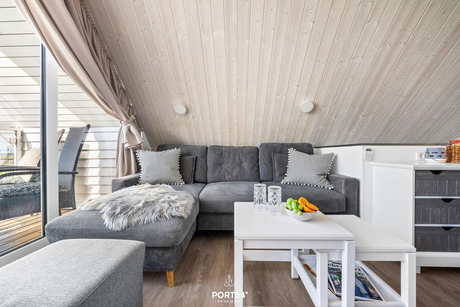 A living area with gray sofa, white table, and wooden ceiling.