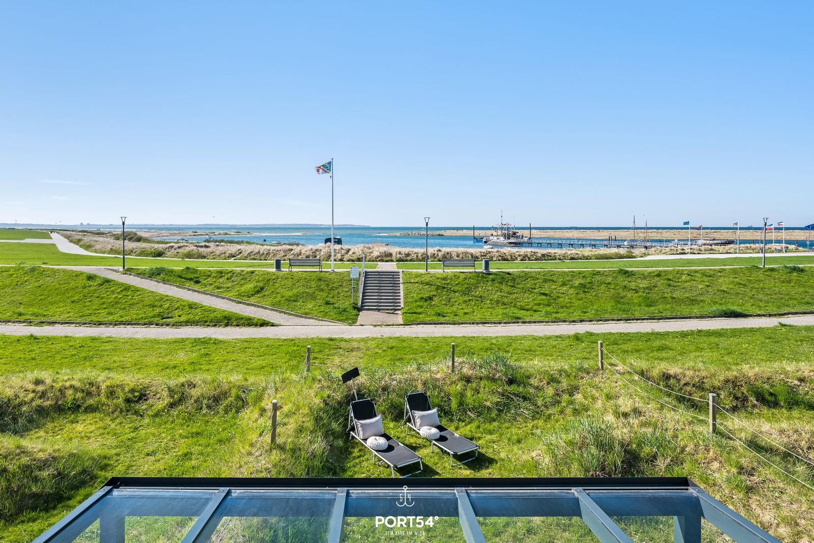Two lounge chairs on green grass with view of harbor and sea.
