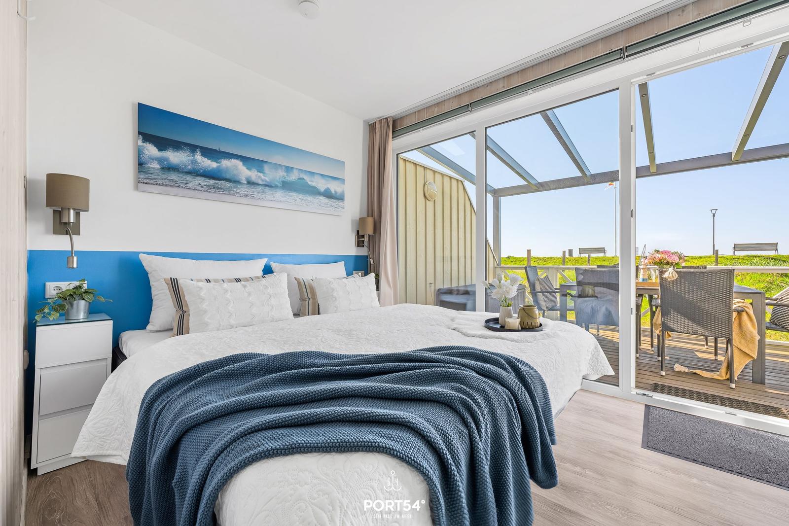 Bedroom with balcony and sea view. Bed with blanket, wall art, and nightstand.