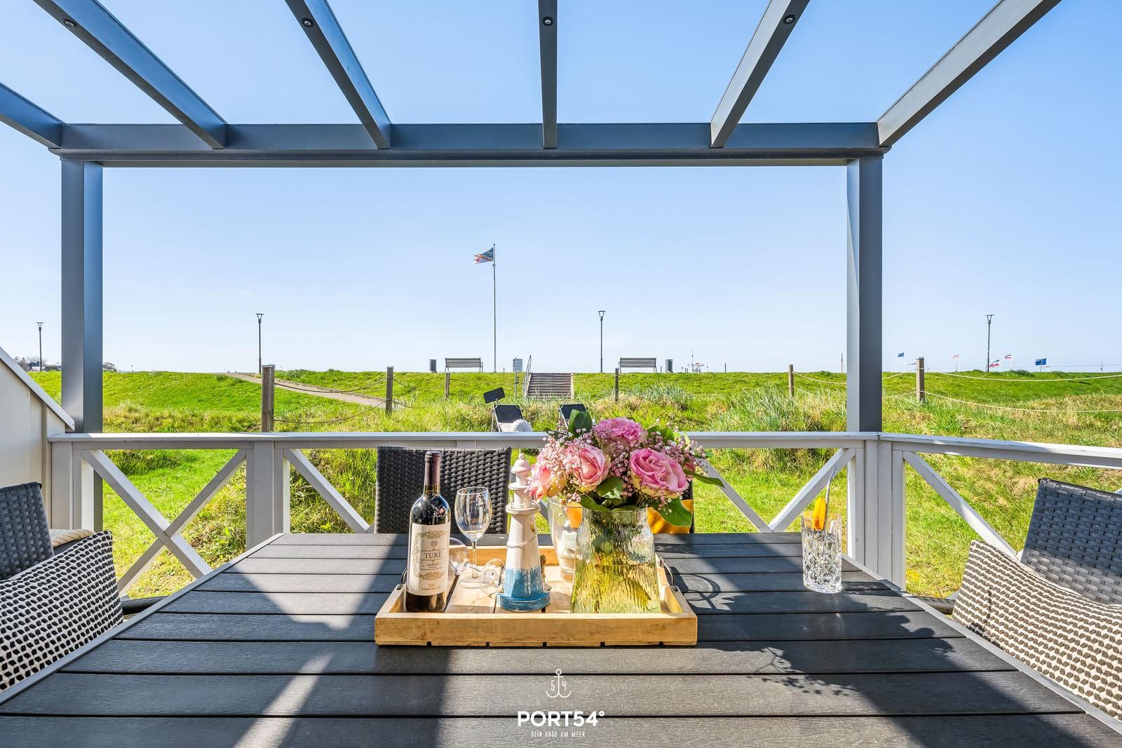 Terrace with table, chairs, and flowers. View of green grass and flag.