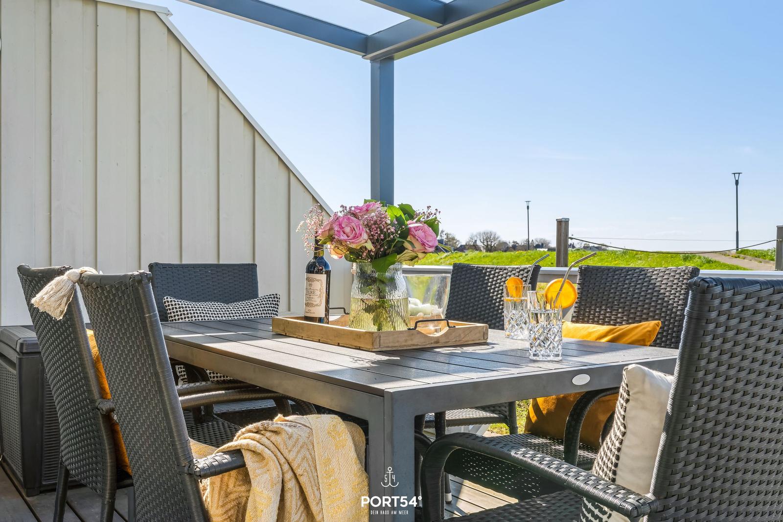 Terrace with table, chairs, and floral arrangement. Background: green field and clear view.