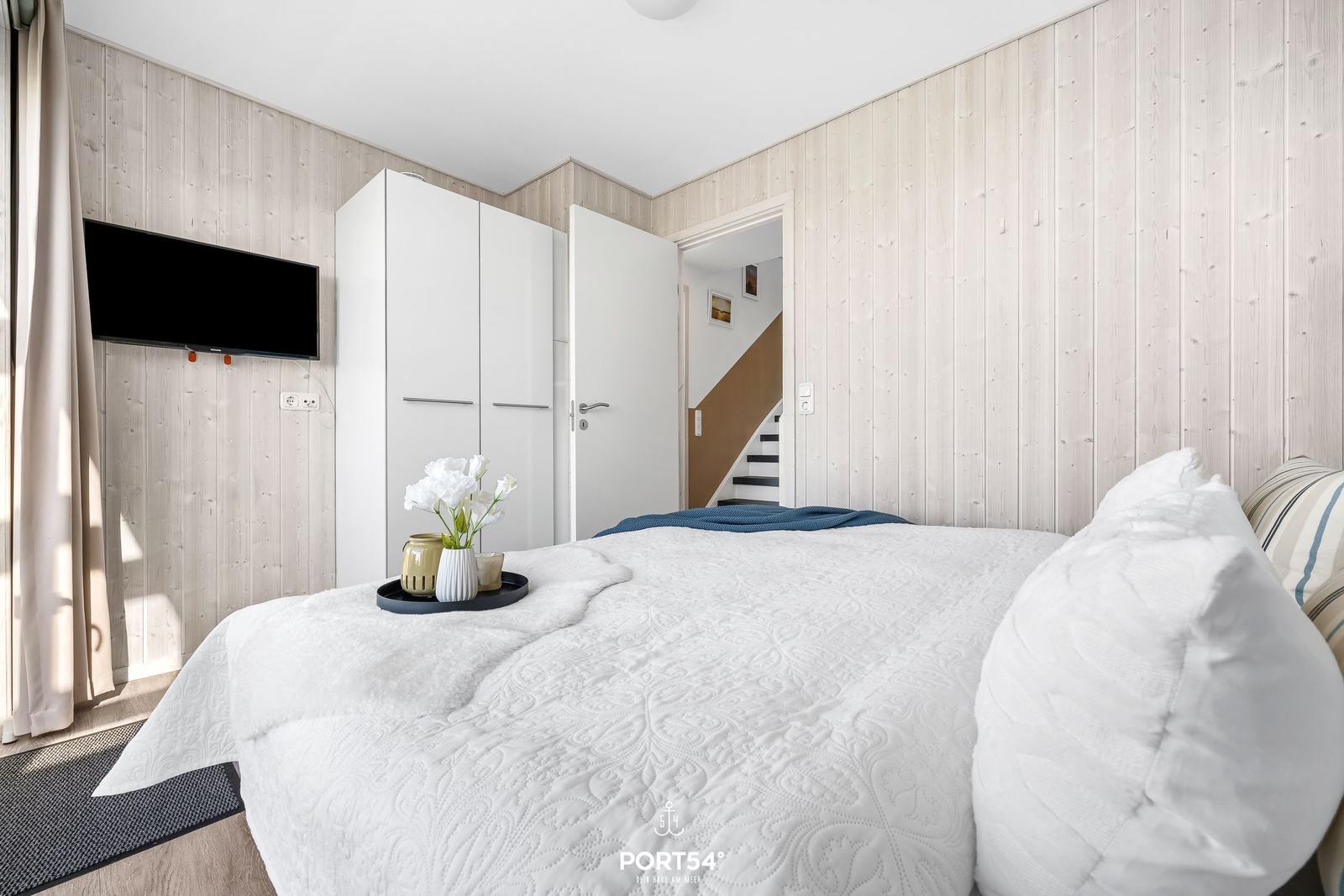 Bedroom with bed, wardrobe, and TV on wood wall