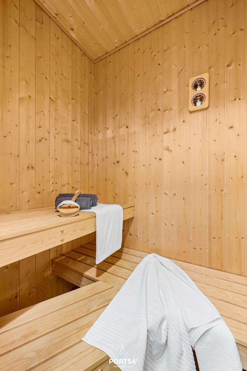 Sauna with wooden bench, towel, and basket. Wall clock and wooden walls visible.