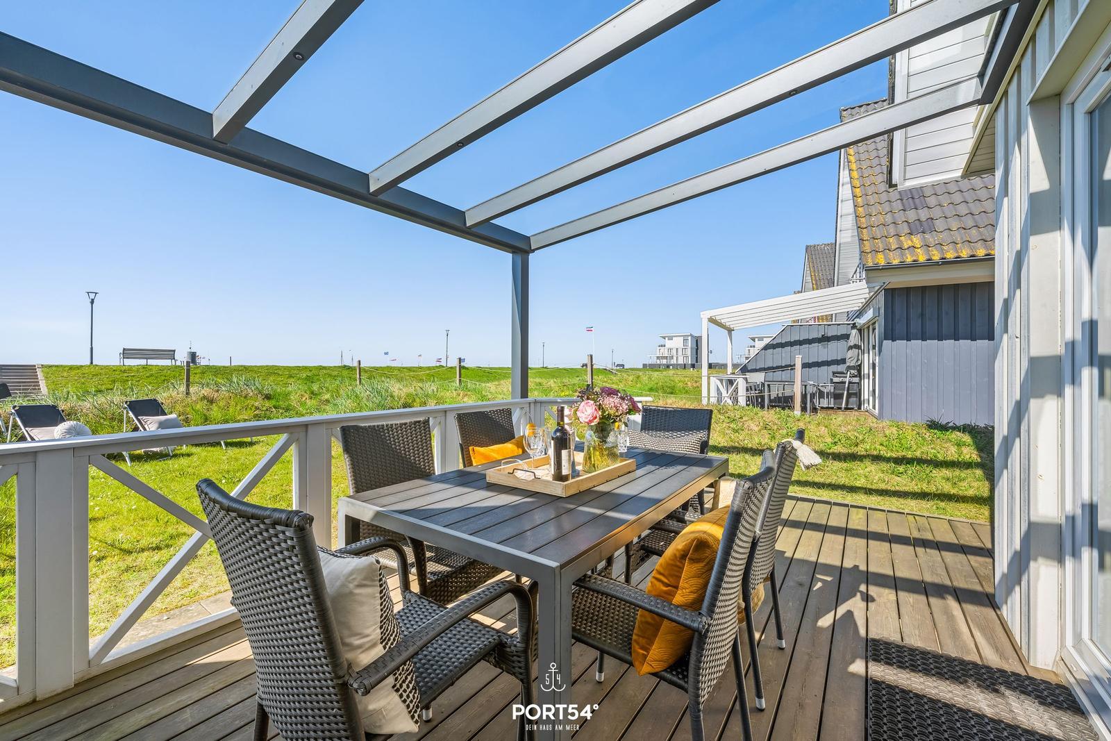 Terrace with table and chairs under glass roof. View of green grass and holiday home.