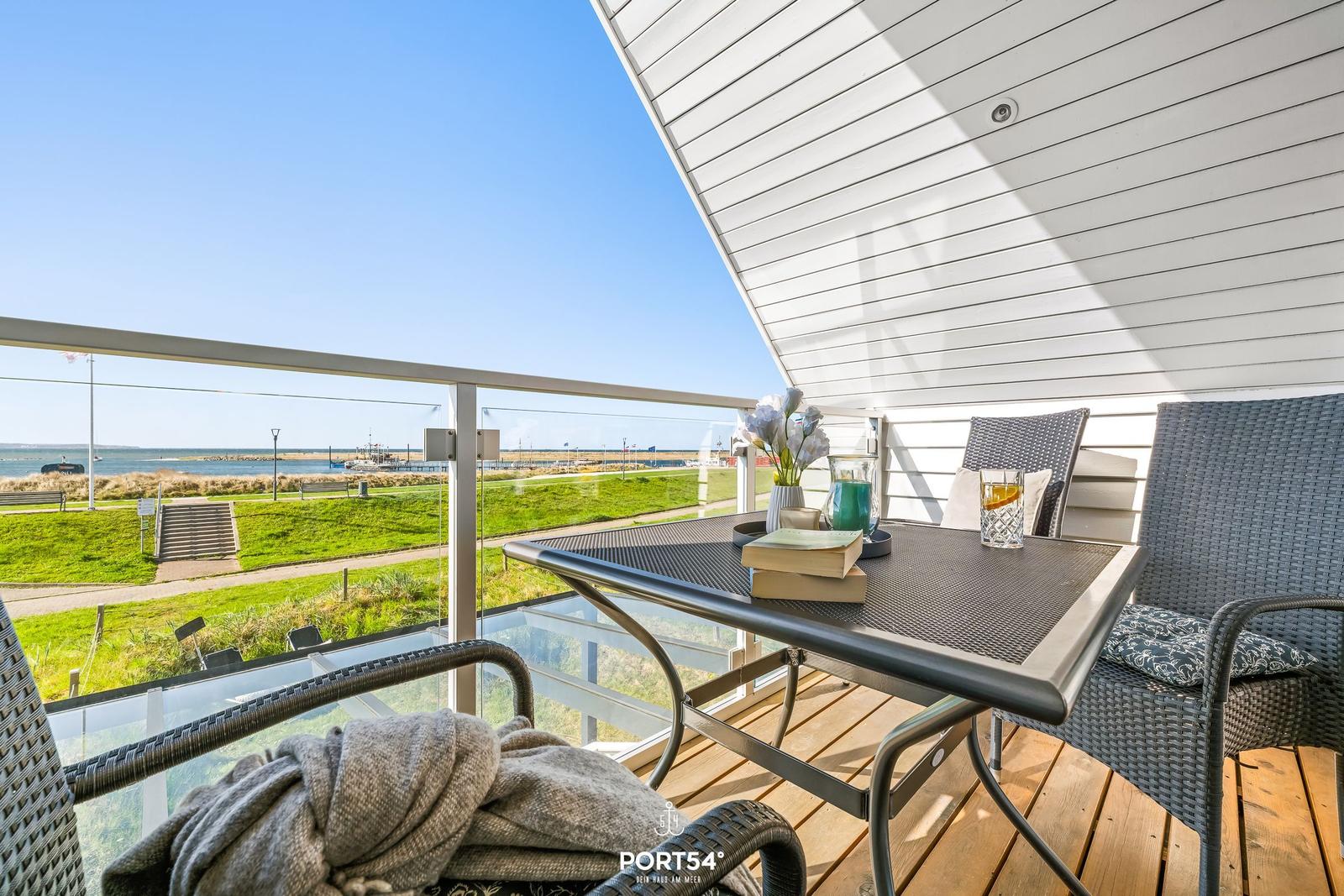 Terrace with table and chairs, view of green area and water.