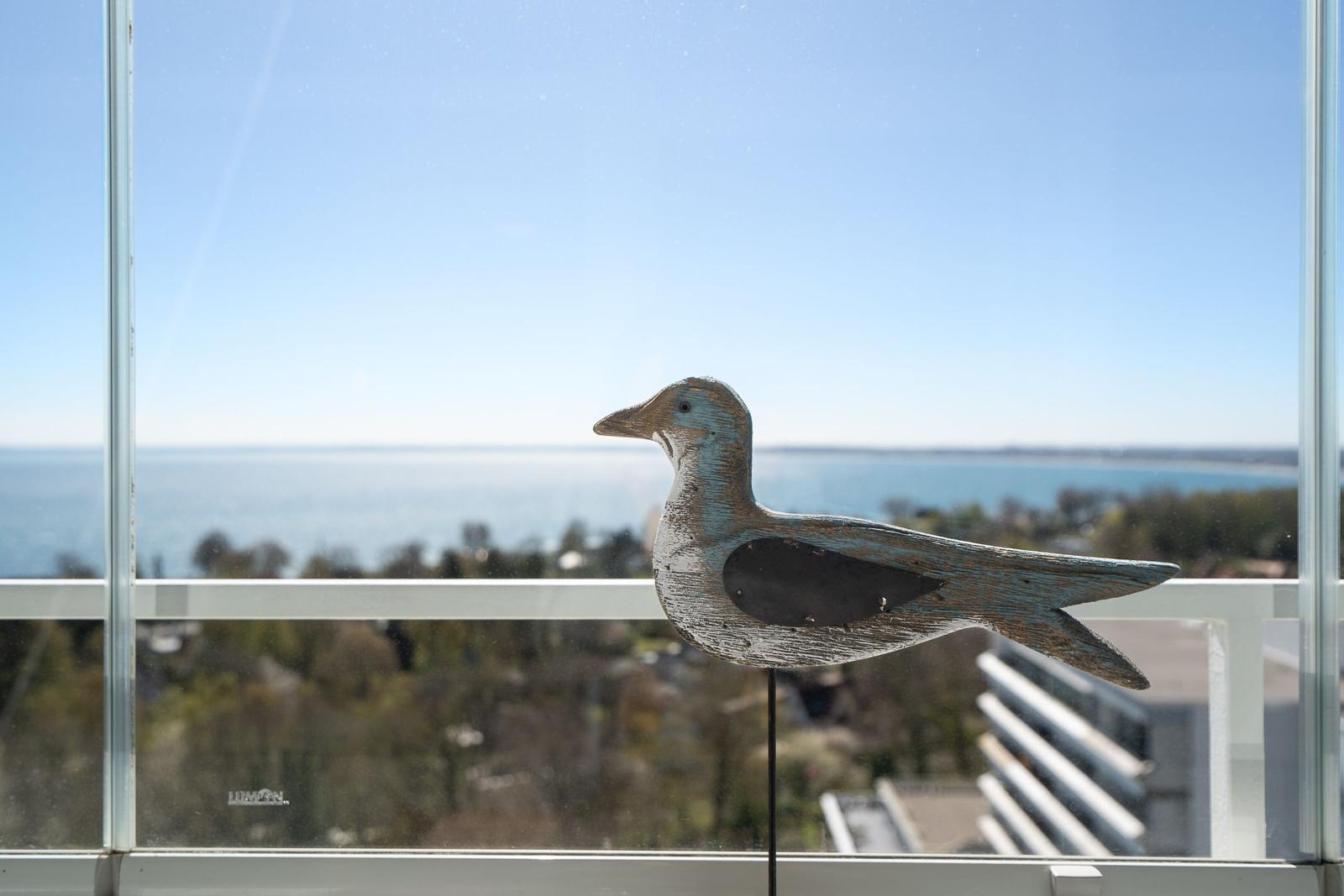 Wooden bird figure in front of a window with sea view.