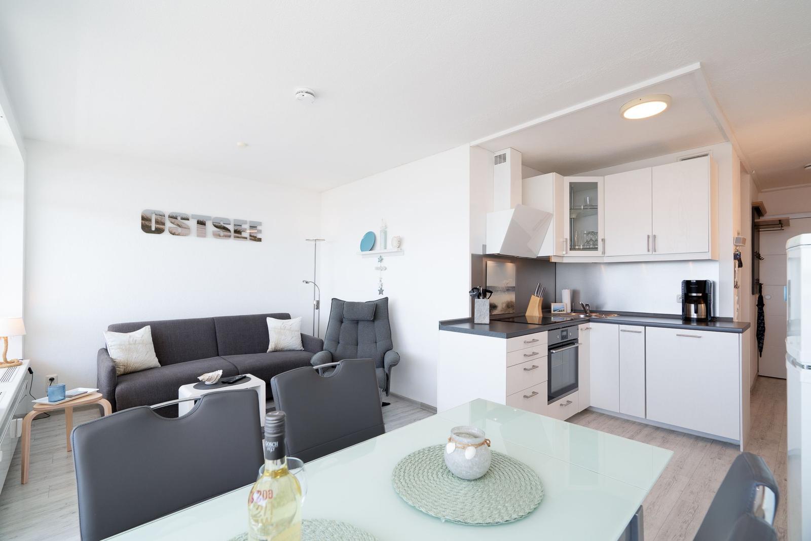 Living kitchen with sofa, dining table, and kitchen cabinets. Wall with OSTSEE sign.