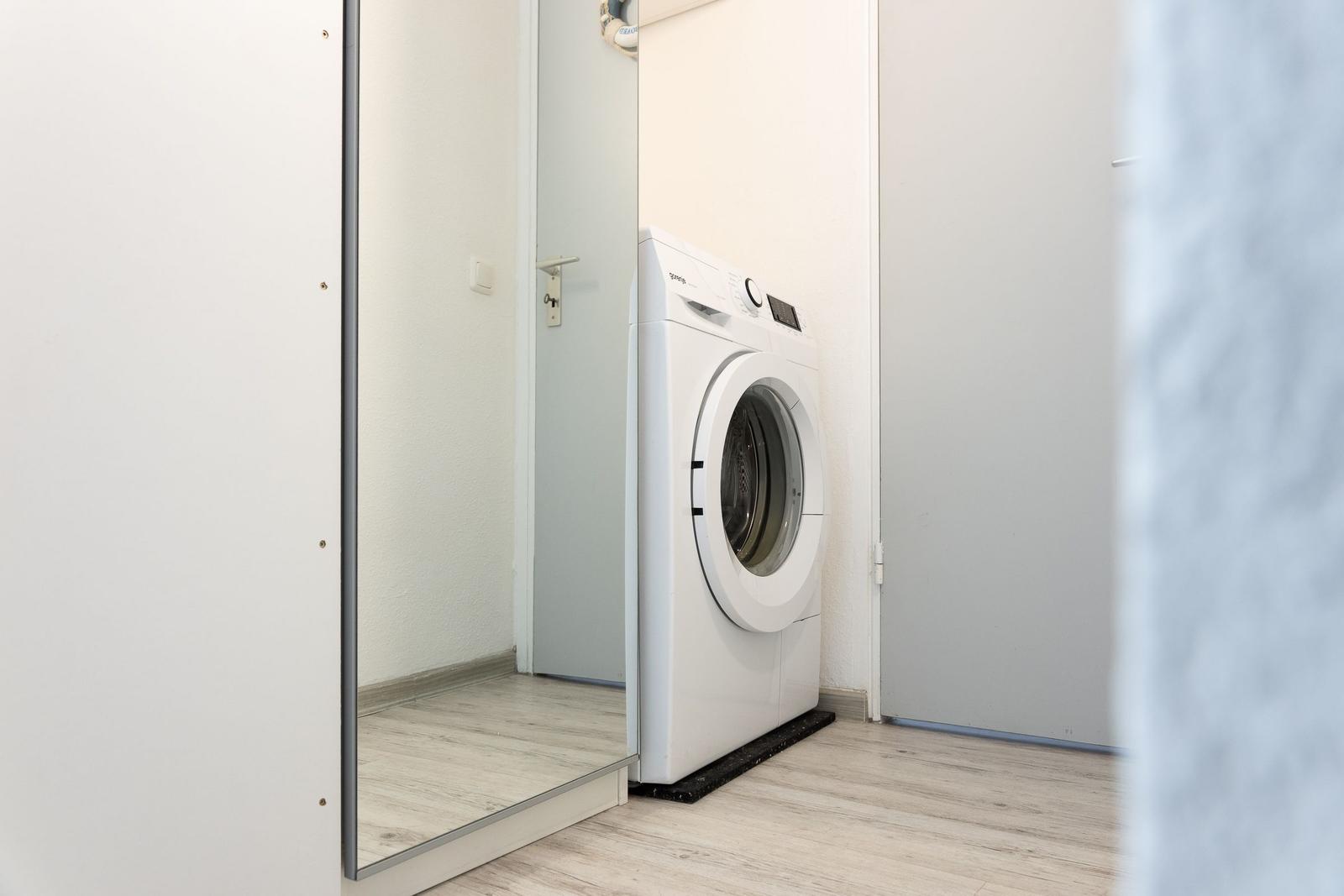Washing machine in a room with wooden floor and mirrored wall.