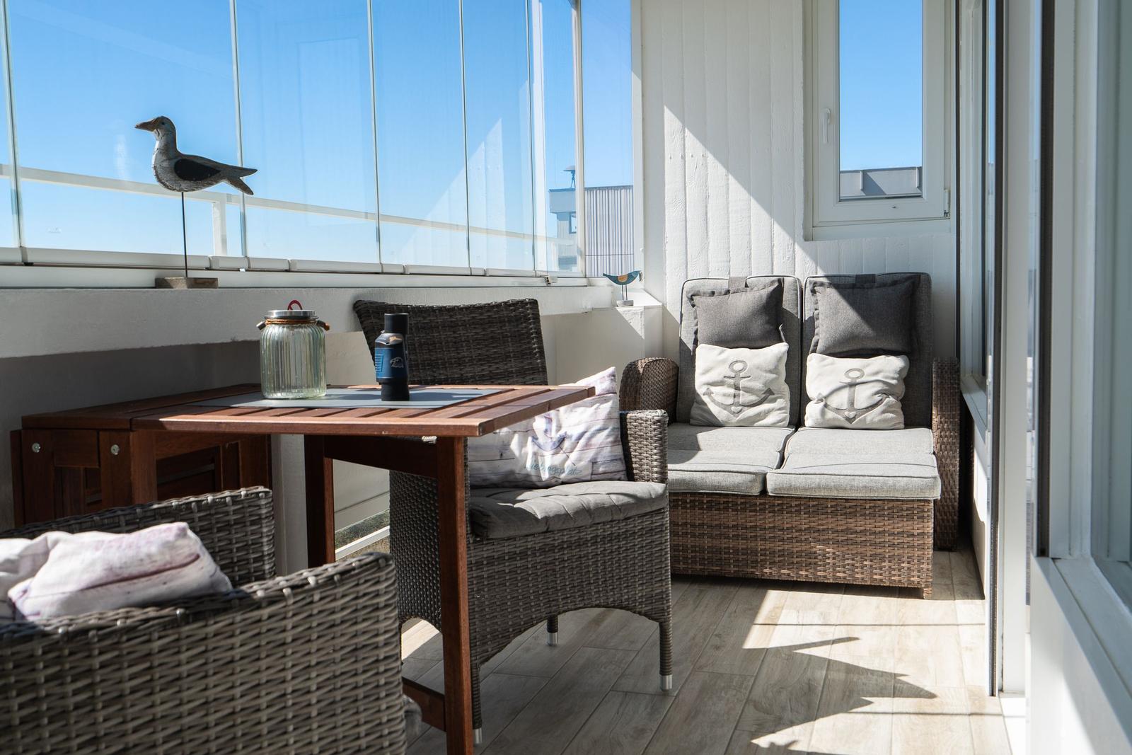 Terrace with seating group, table, and sea view through glass wall.