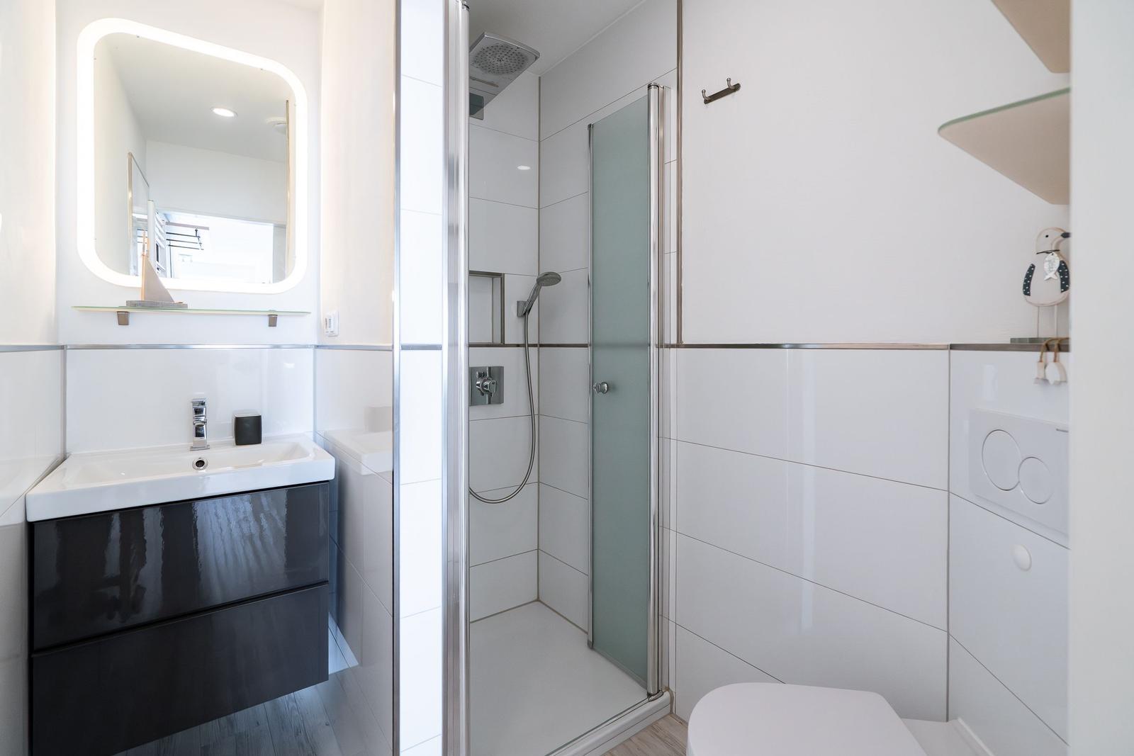 Bath with shower, sink, and toilet. Modern setup with glass partition and lit mirror.