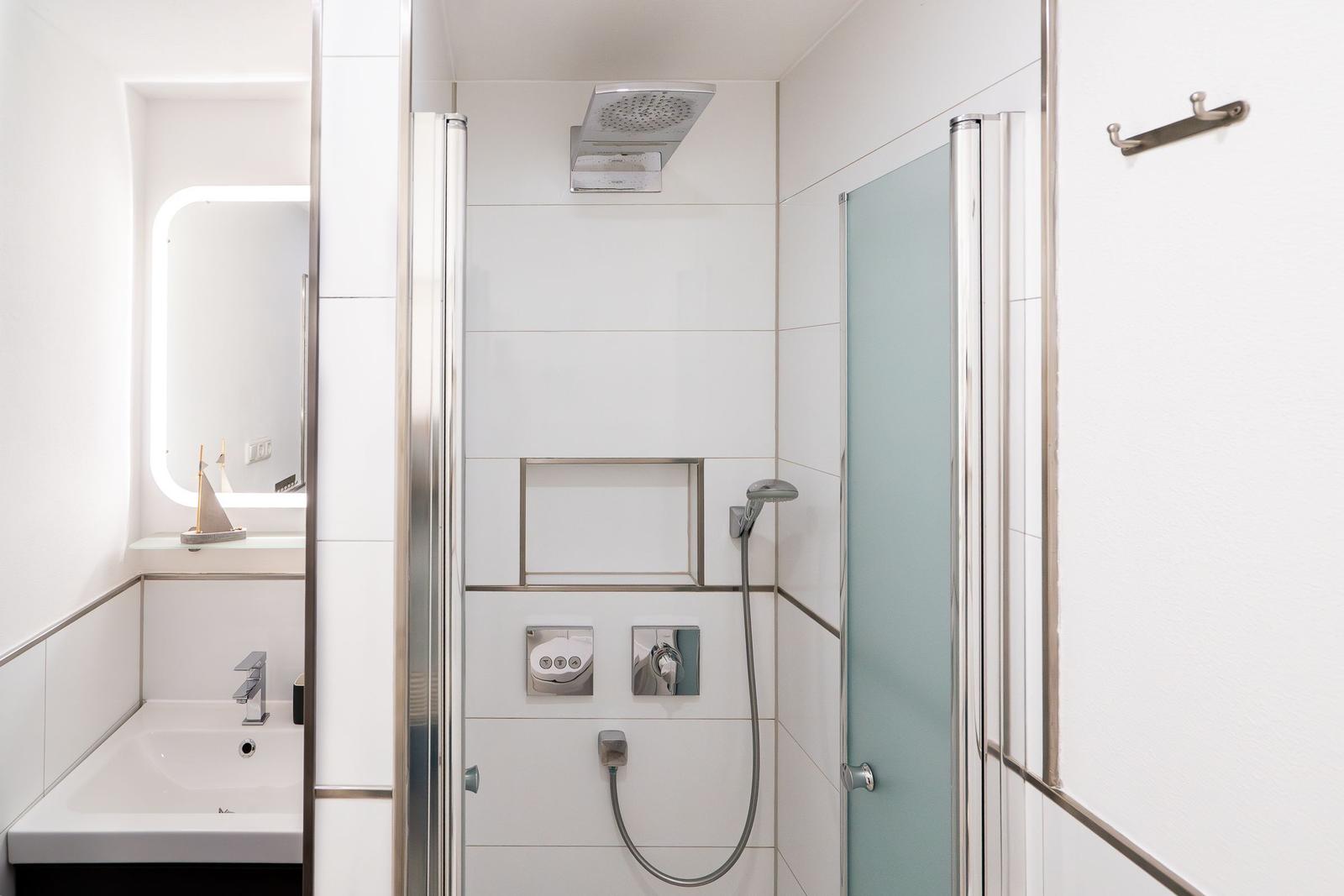 Shower with overhead and handheld shower, sink with mirror and small sailboat decoration.