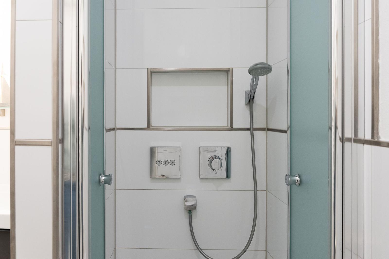 Shower with showerhead, controls, and built-in shelf on white tiled walls.