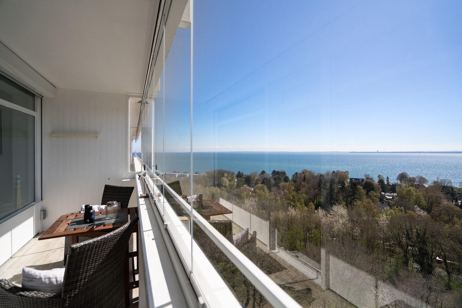 Terrace with table and chairs offers view of sea and trees.