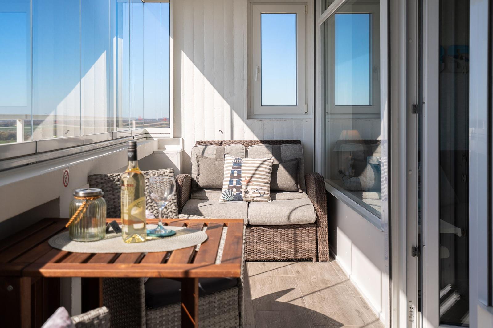 Terrasse mit Sitzgruppe, Tisch und Getränken. Glaswand und Fenster bieten Aussicht.