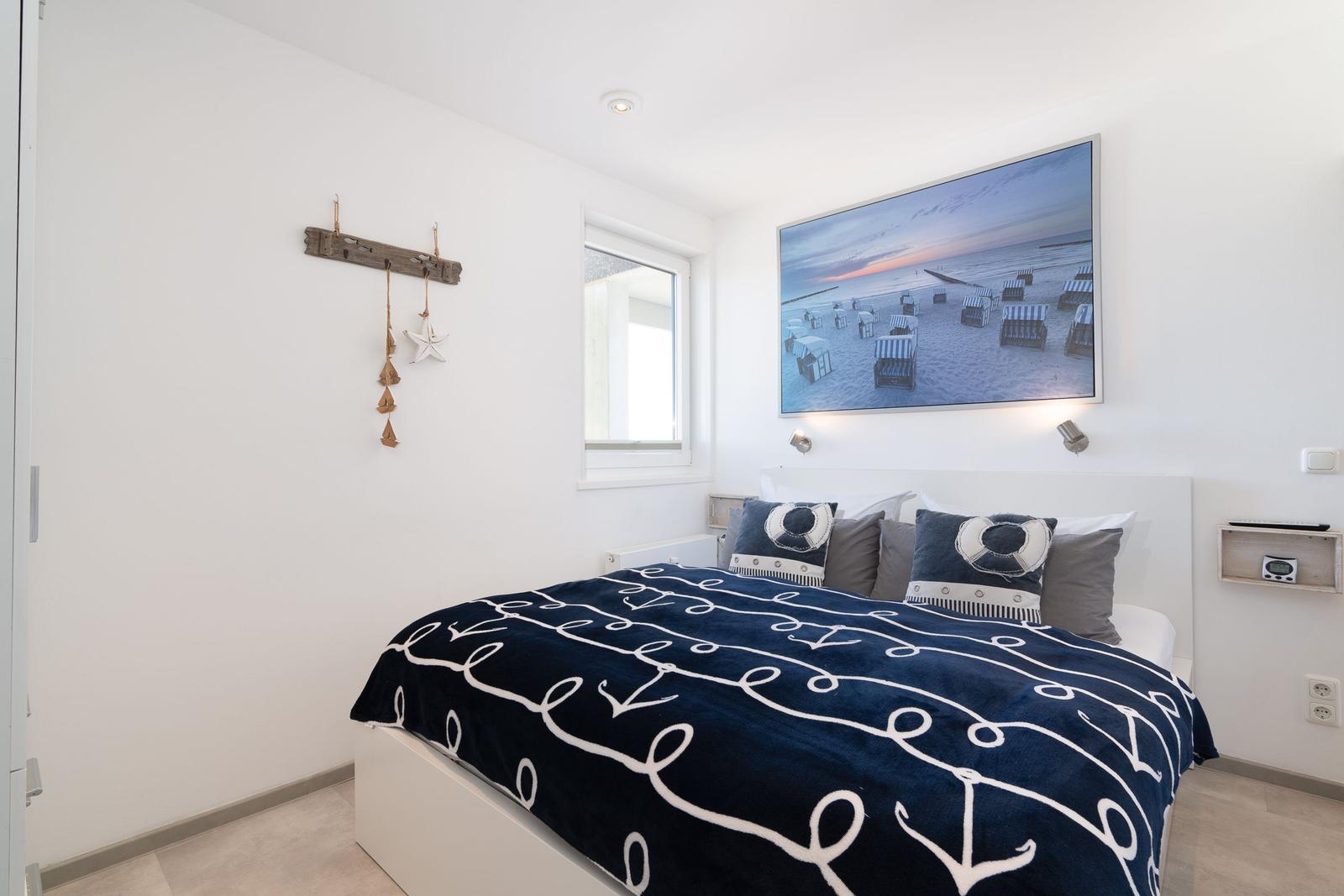 Schlafzimmer mit Bett, Wandbild und Fenster. Dekoration mit Strandmotiven.