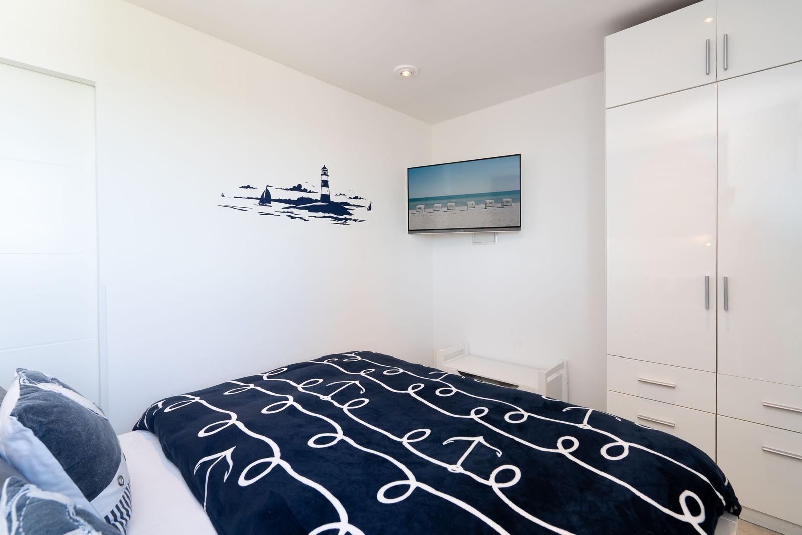 Schlafzimmer mit Bett, Kleiderschrank und Wandbild mit Leuchtturm.
