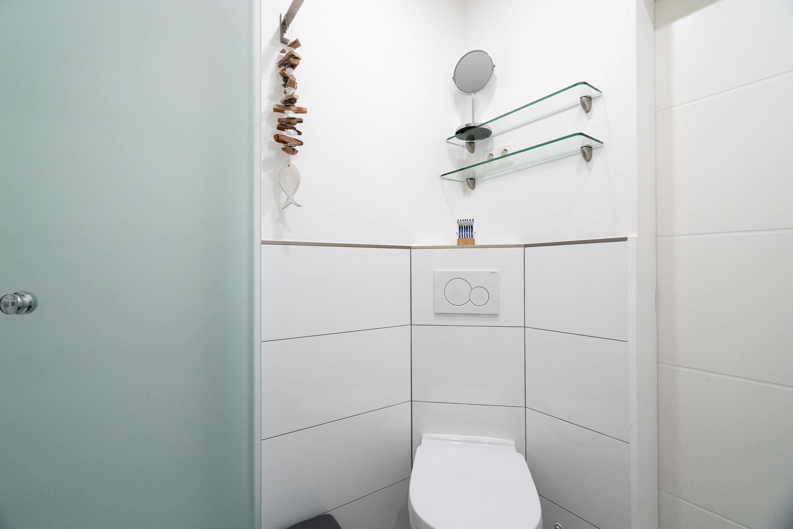 Dusche mit Toilette, Glasregalen und Spiegel an der Wand.