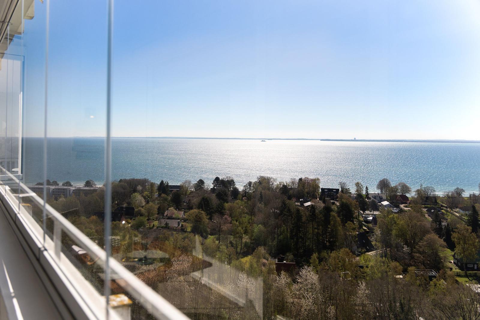 Blick vom Balkon auf See und grüne Landschaft mit Bäumen und Häusern.