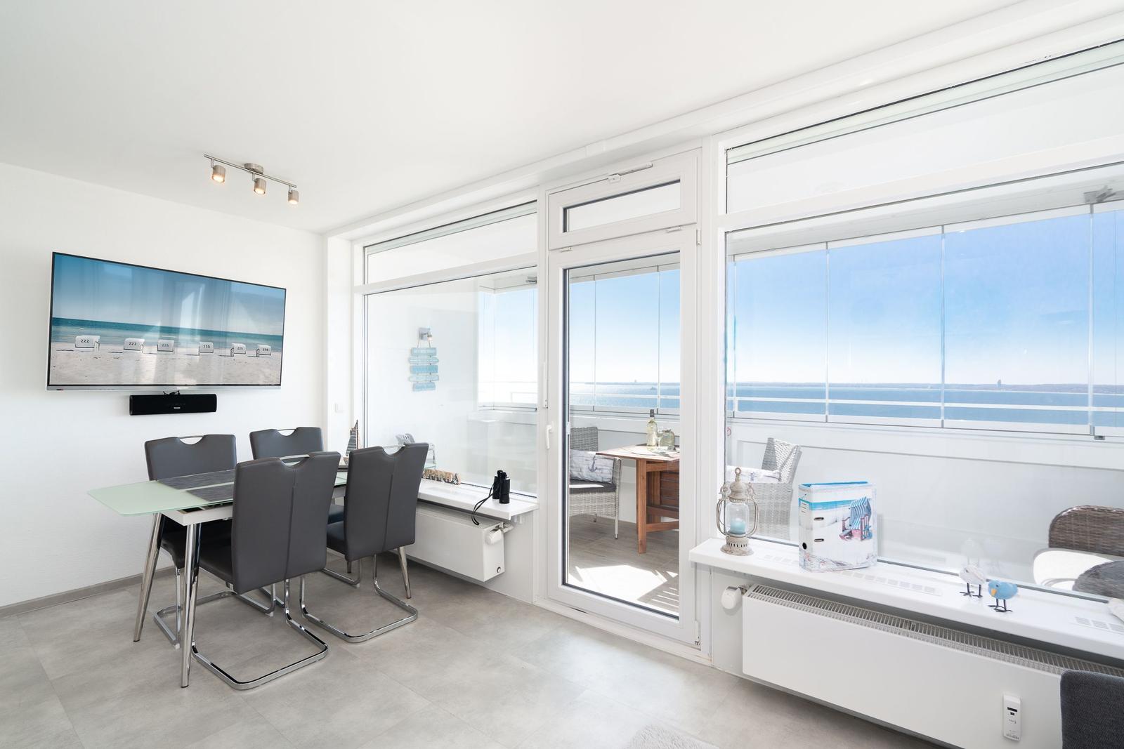 Essbereich mit TV und Blick aufs Meer über große Fenster.