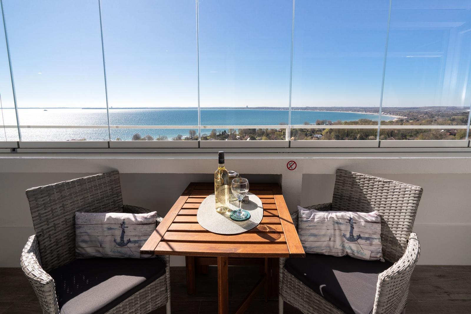 Terrasse mit Tisch und zwei Stühlen, Blick auf Meer und Strand.
