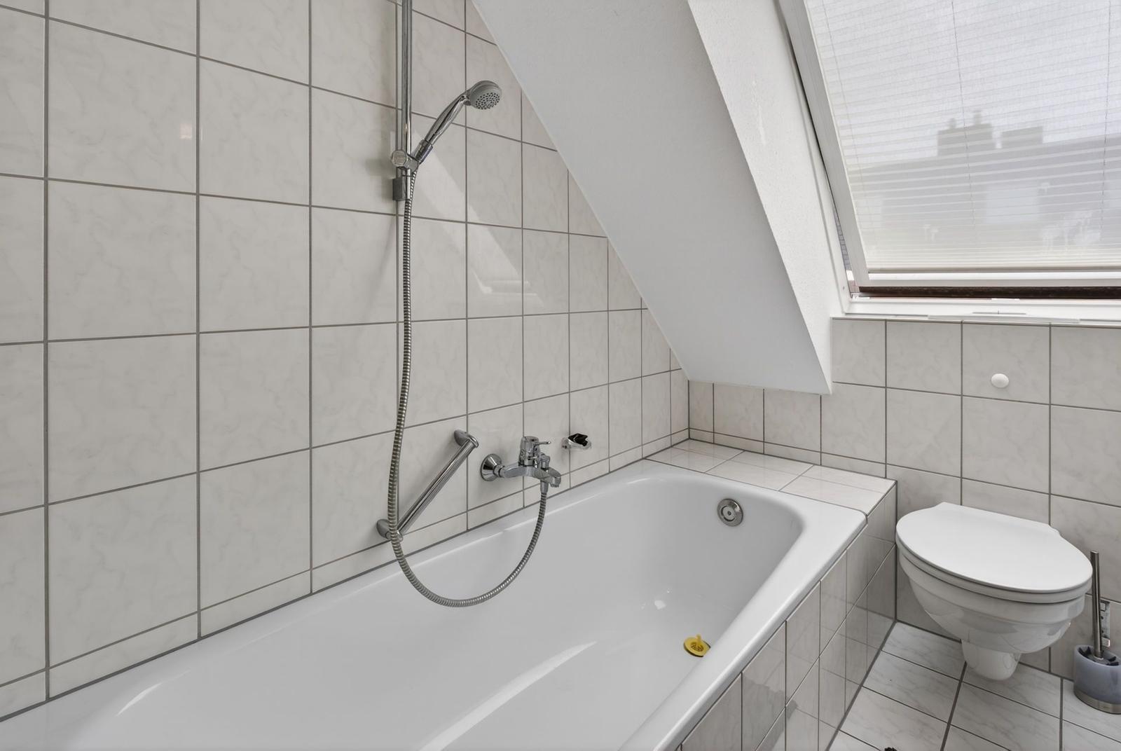 Bathroom with bathtub, shower, and toilet under sloped ceilings.