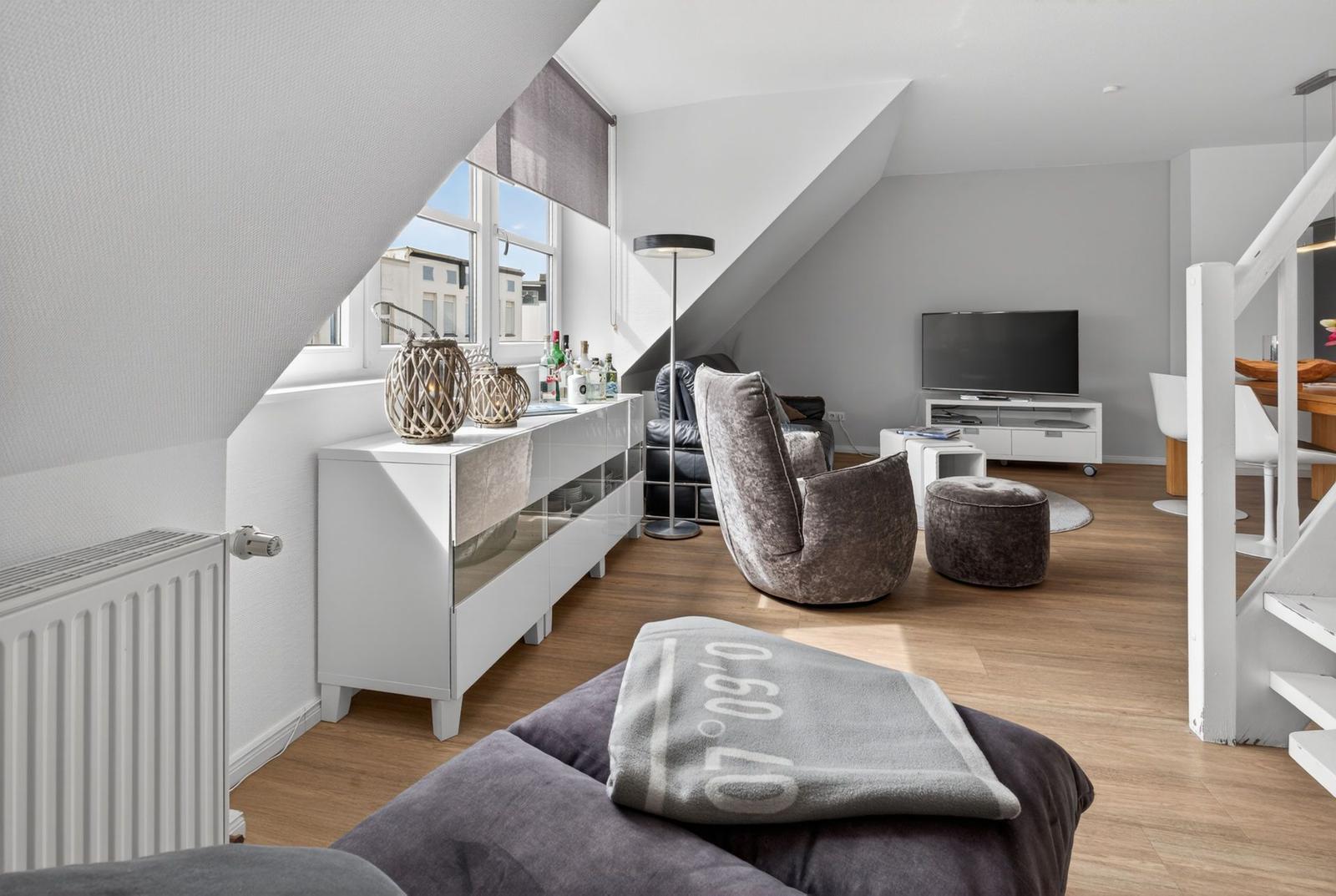 Living room with sloped ceiling, sofa, TV, and wooden floor.