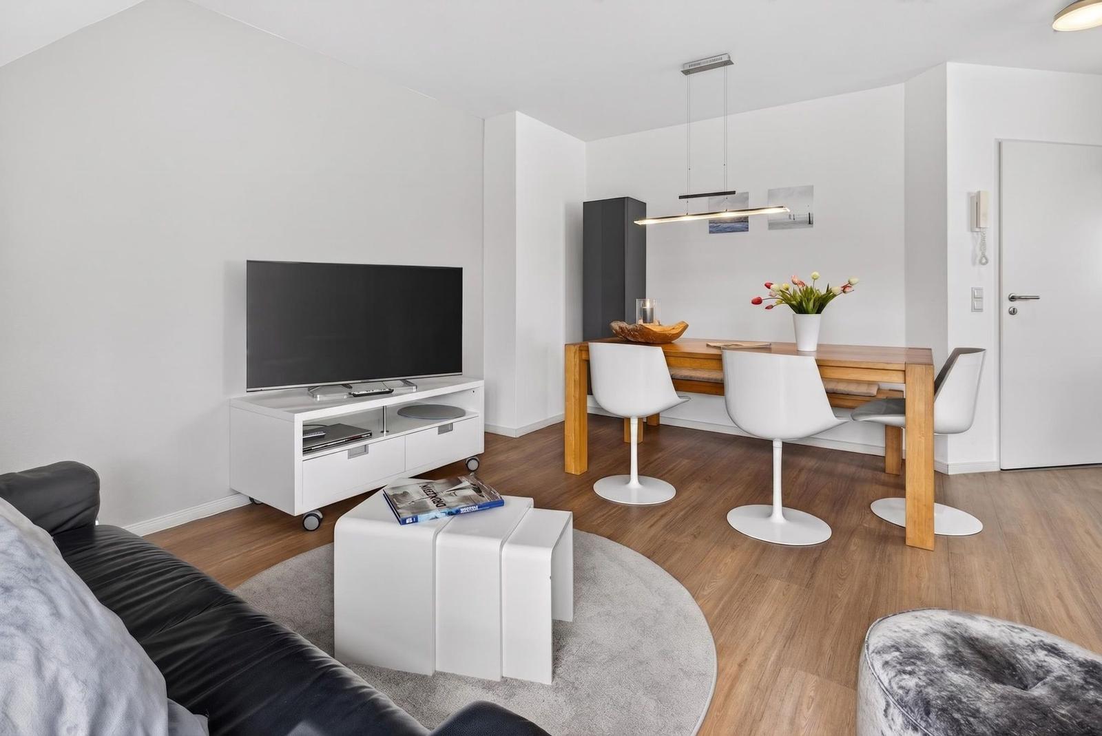 Living and dining area with TV, table and chairs on wooden floor.