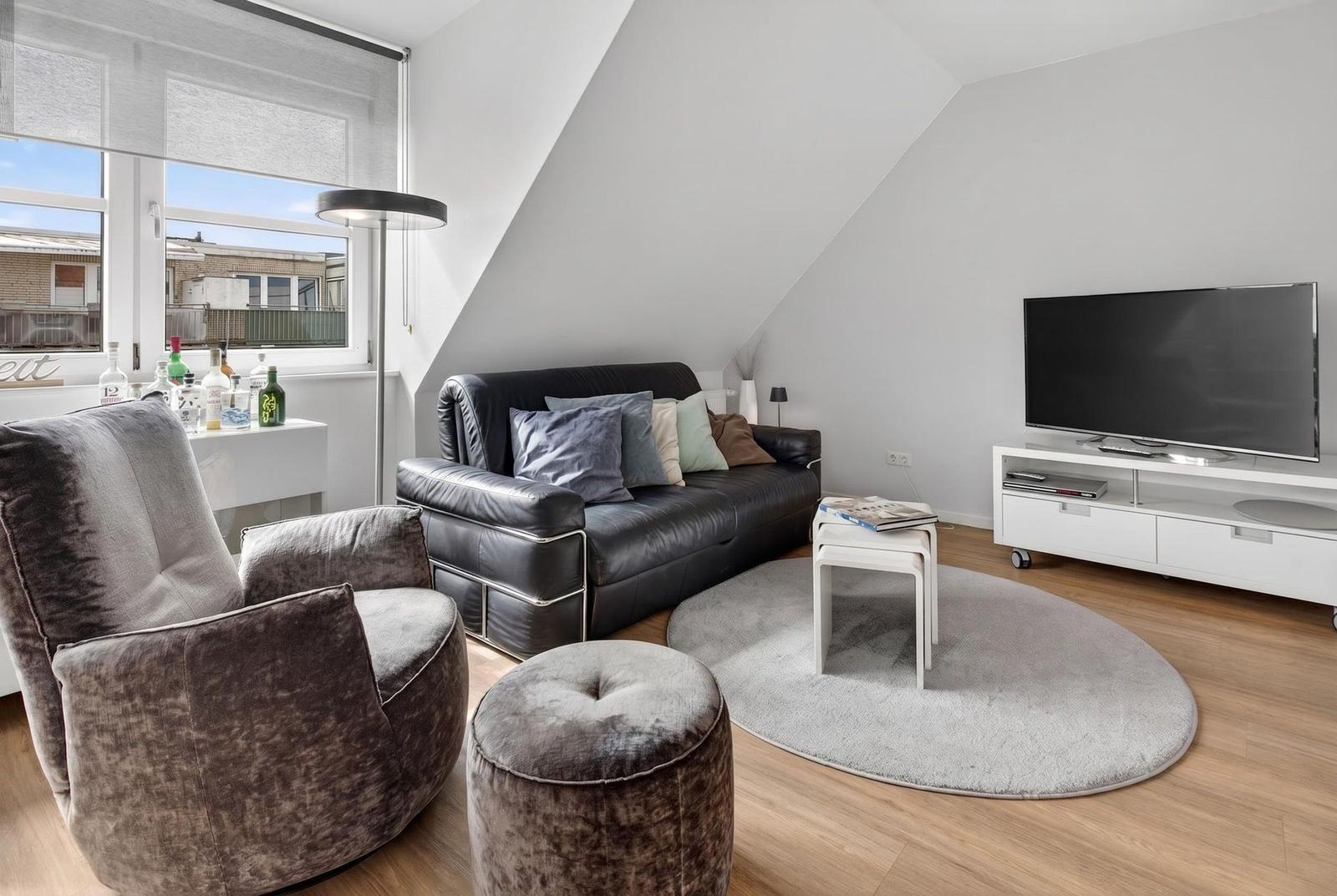Living room with sofa, armchair, TV, and round rug.