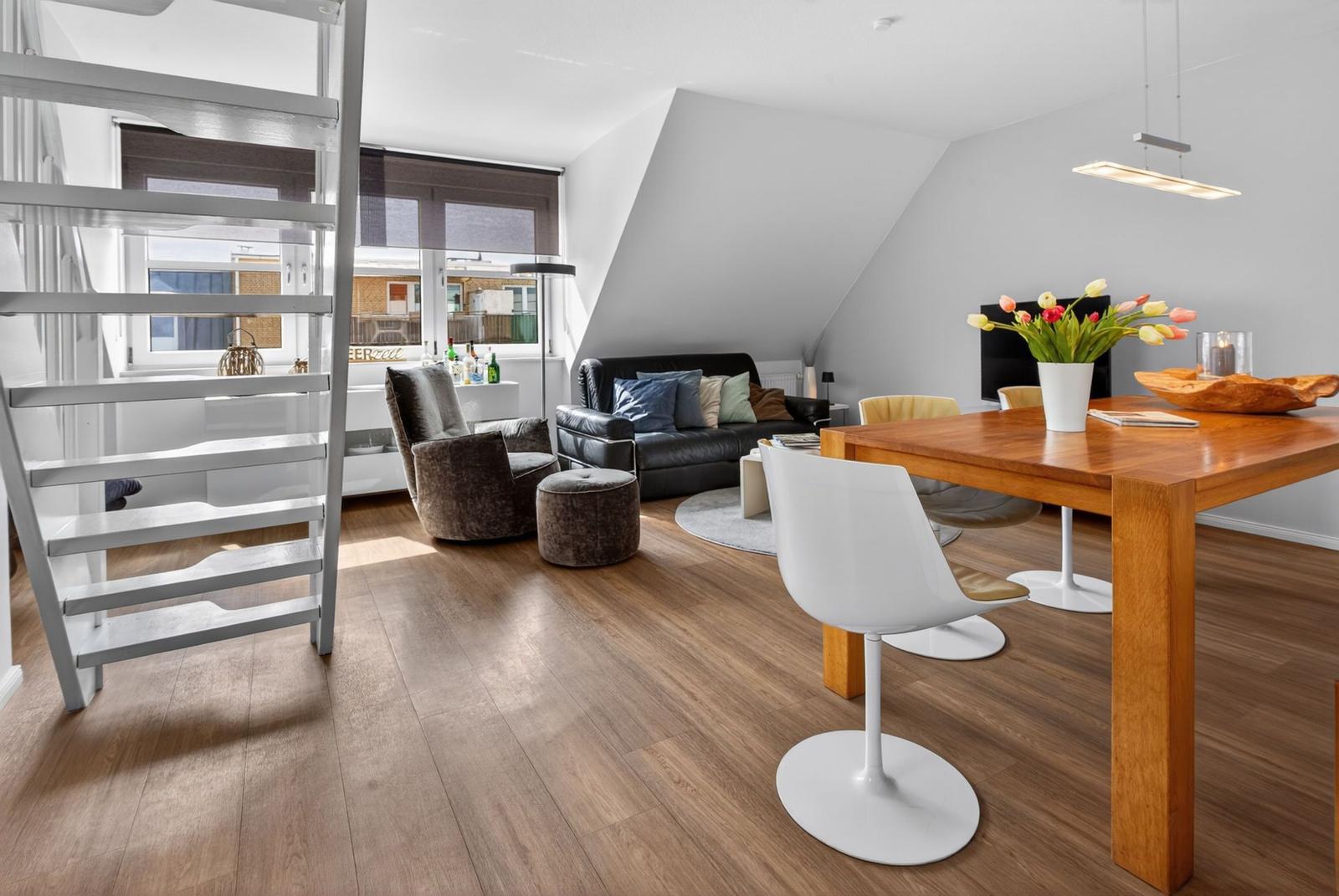 Living and dining area with wooden floor, table, chairs, and staircase.