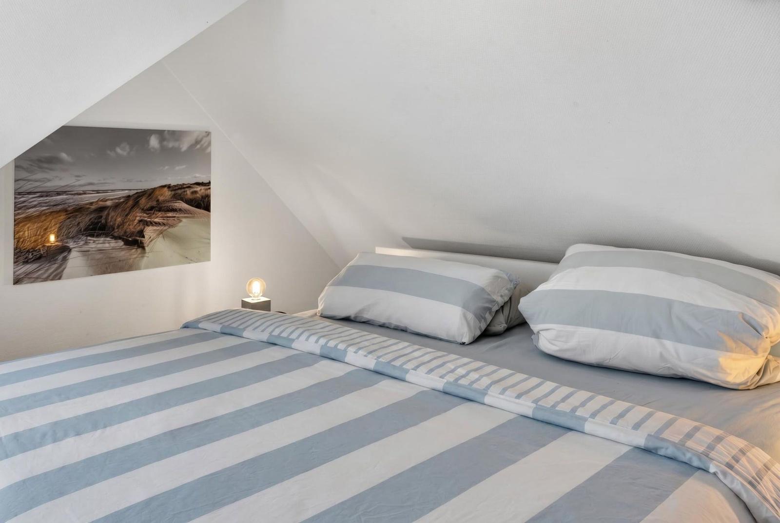 Bedroom with sloped ceiling, bed with striped cover, and wall art.