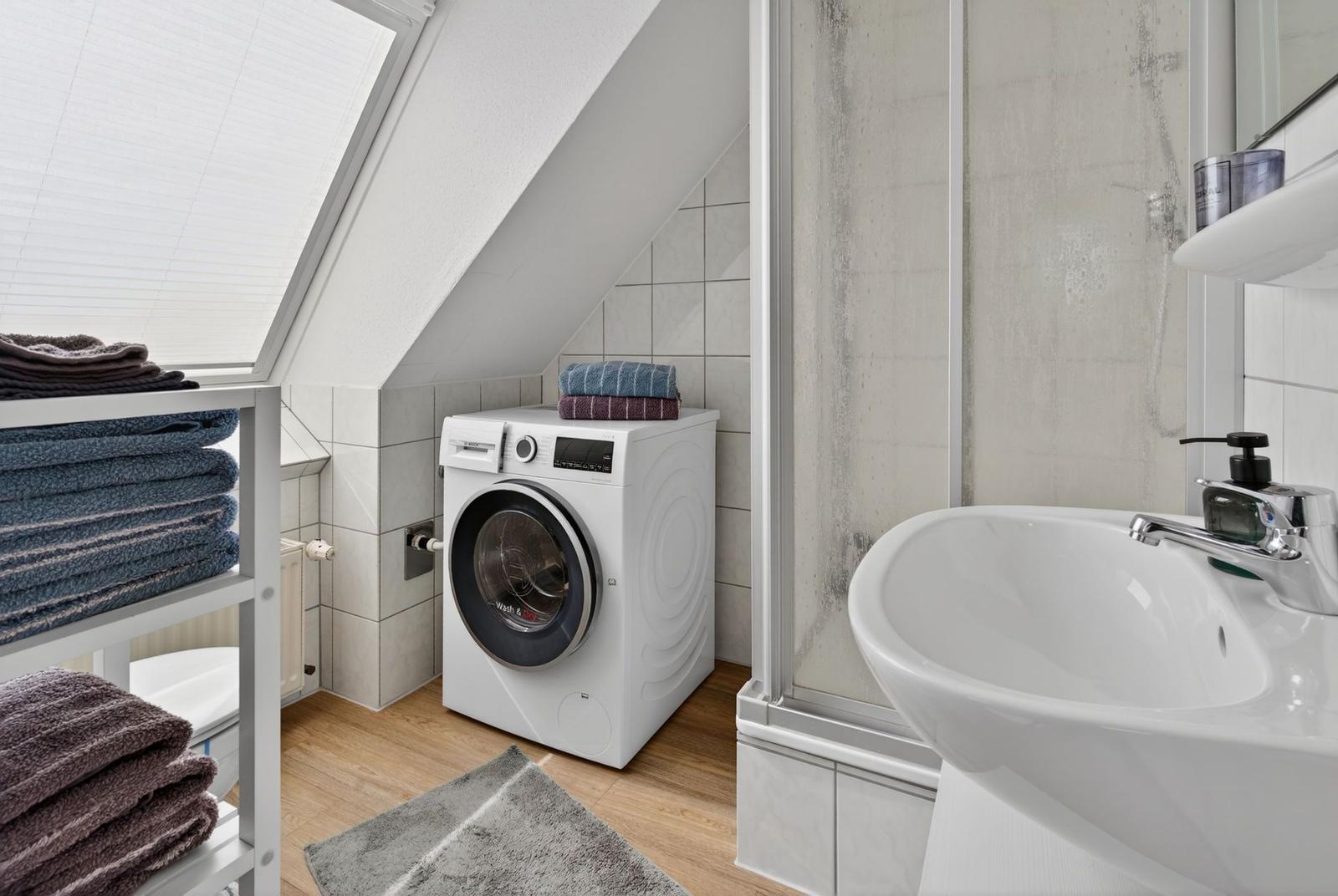 Bathroom with washing machine, sink, and shower under sloped ceiling.