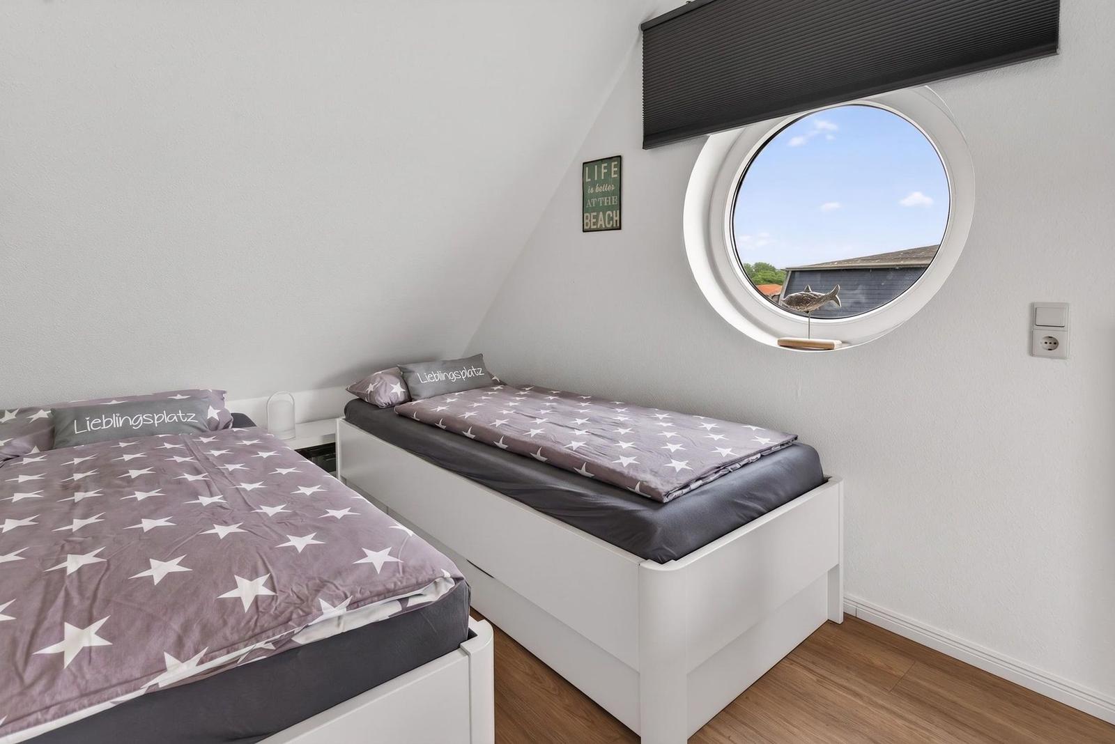 Two beds with star-patterned bedding and round porthole window in an attic room.