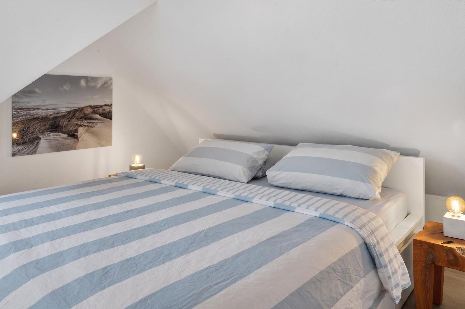 Bedroom with double bed, striped bedding, and wall art on sloped ceiling.