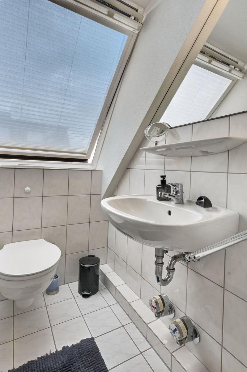 Bathroom with sink, toilet, and skylight. Tiled walls and floor.