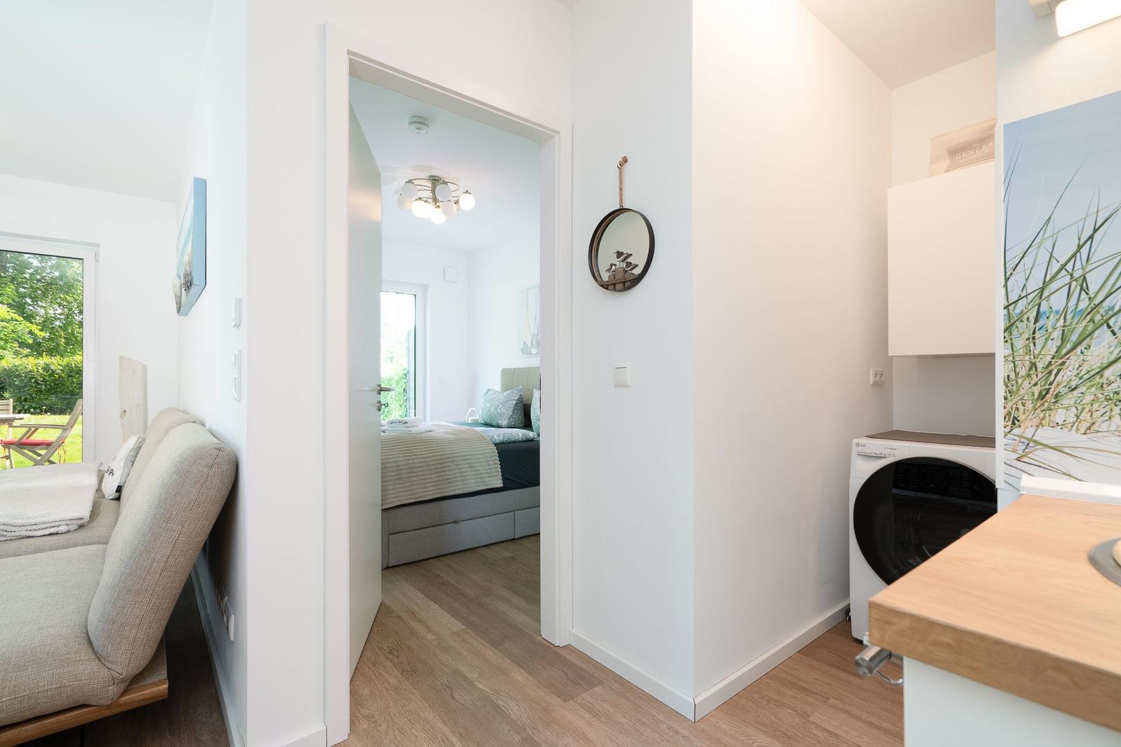 Living area with bedroom and washing machine. Wooden floor and white walls.